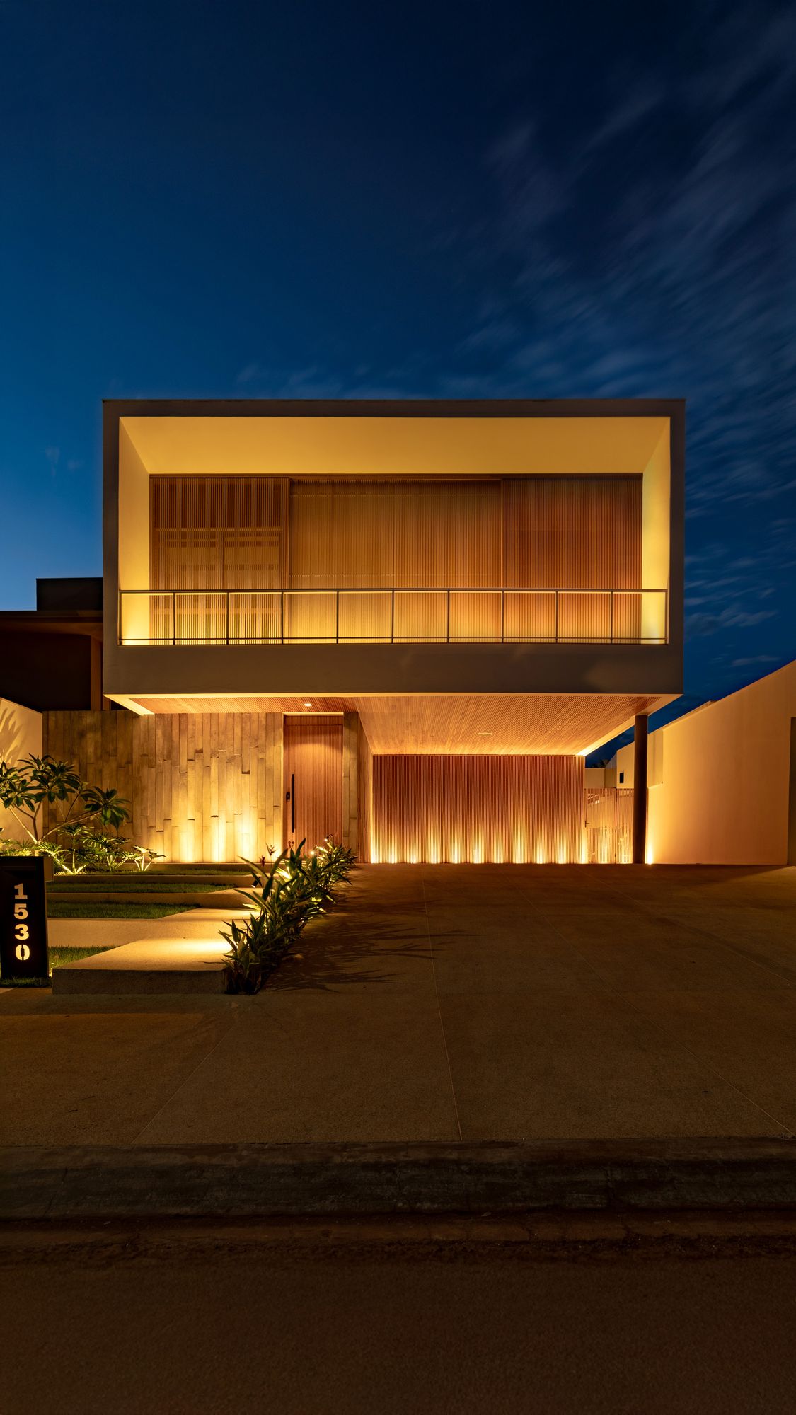 Fachada da Casa MPG ao anoitecer, com volume em madeira iluminado